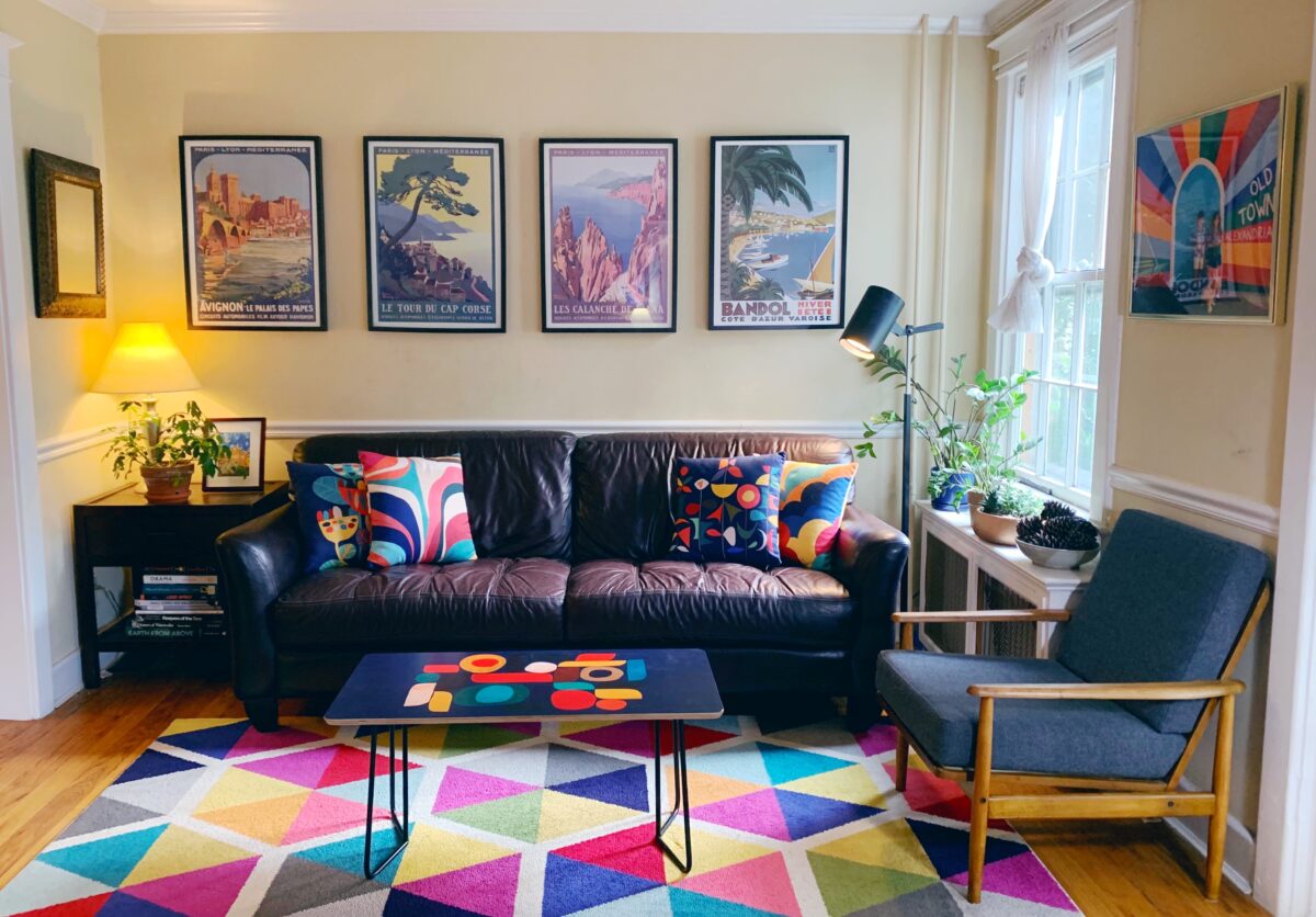 Living room with a color block rug, wooden chair with a blue cushion, maroon couch, and graphic national park art on the walls