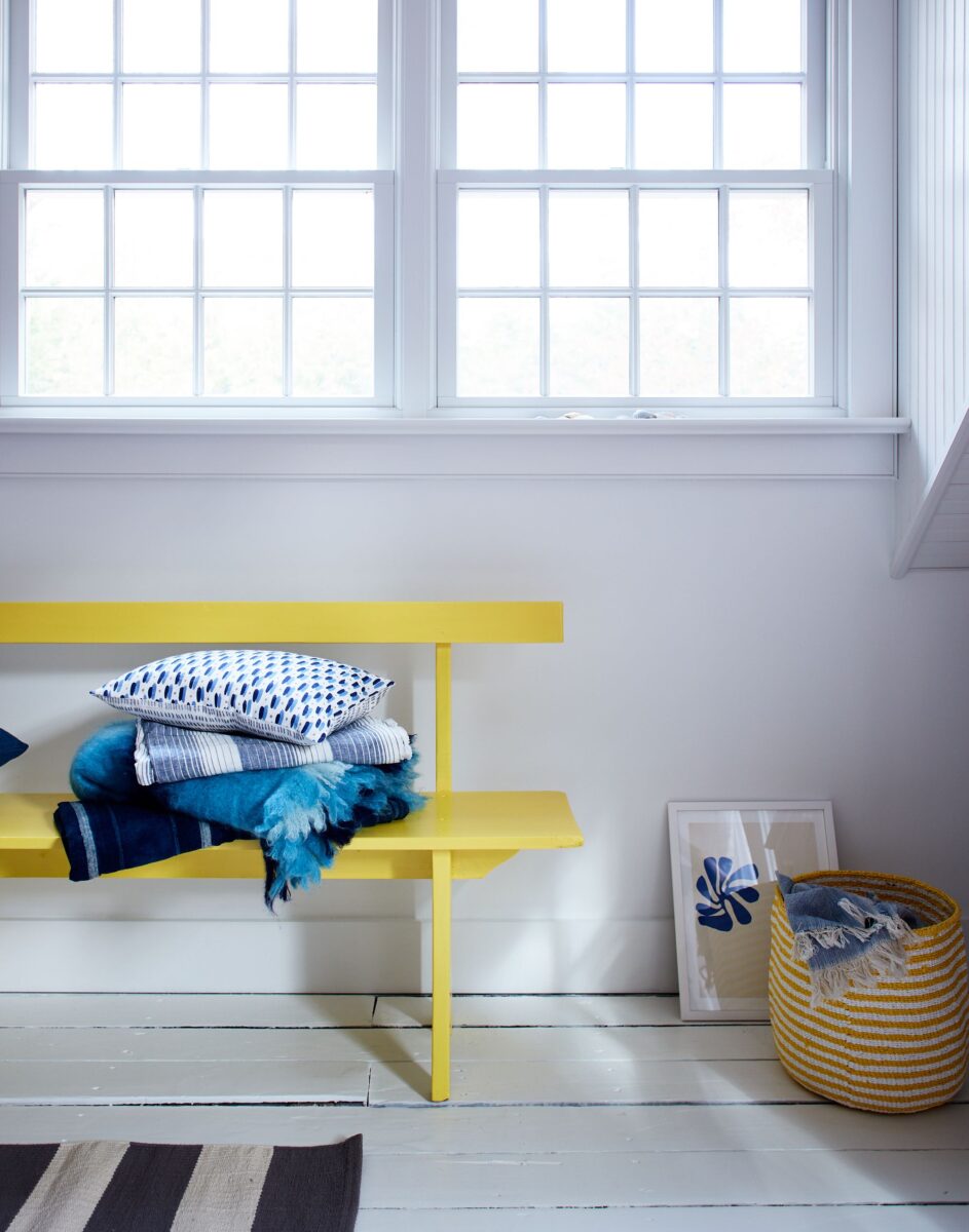 A vibrant yellow bench sits in front of a white wall. 