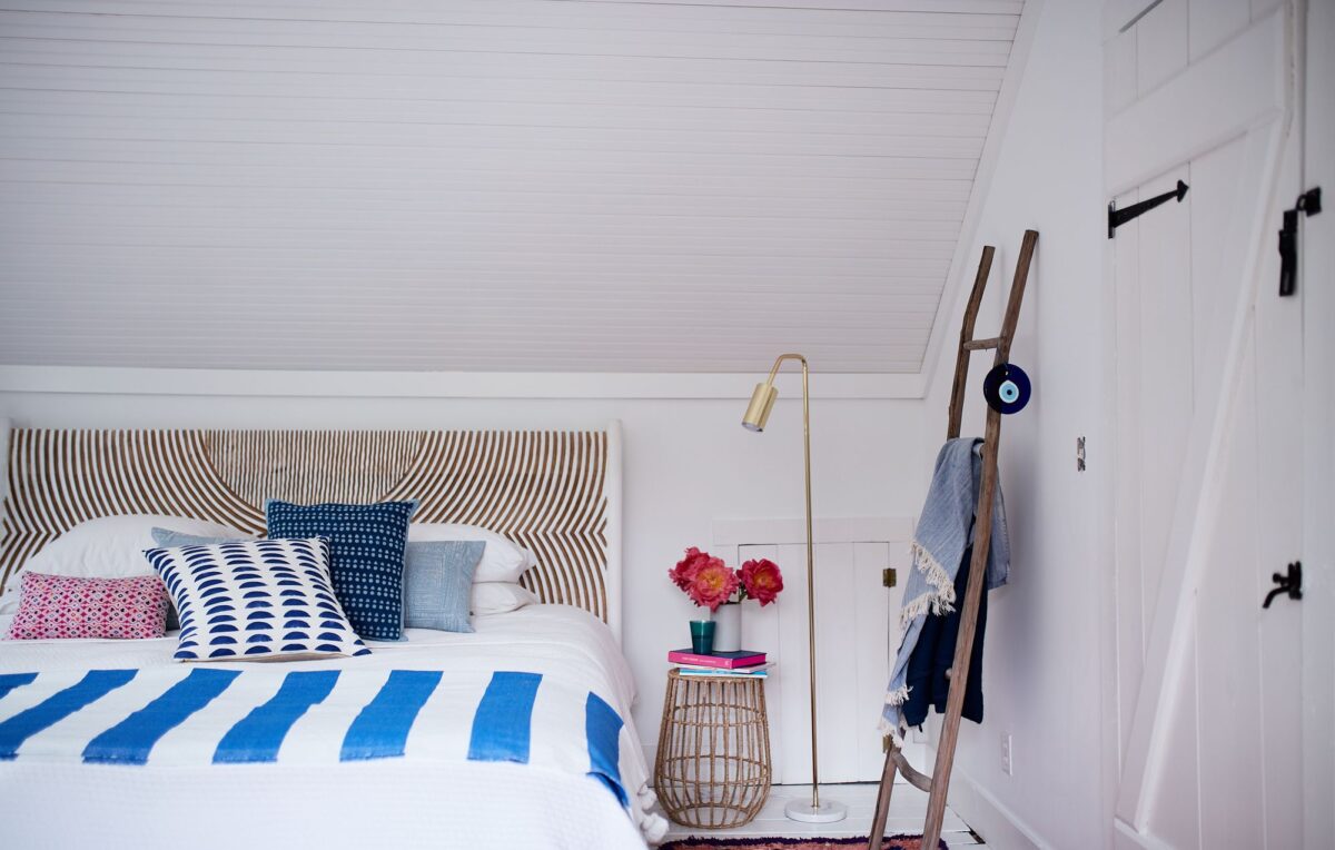 A bedroom with crisp white sheets, striped blue blanket, and bright pink roses on the bedside table.