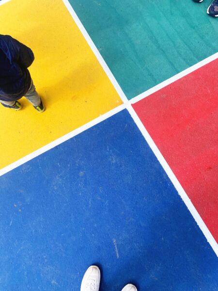 A foursquare grid with the colors red, yellow, green, and blue seen from above with adult and child's feet