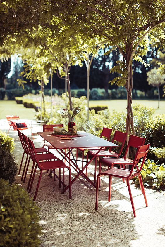 Red outdoor dining set by Fermob under a grove of vines. 