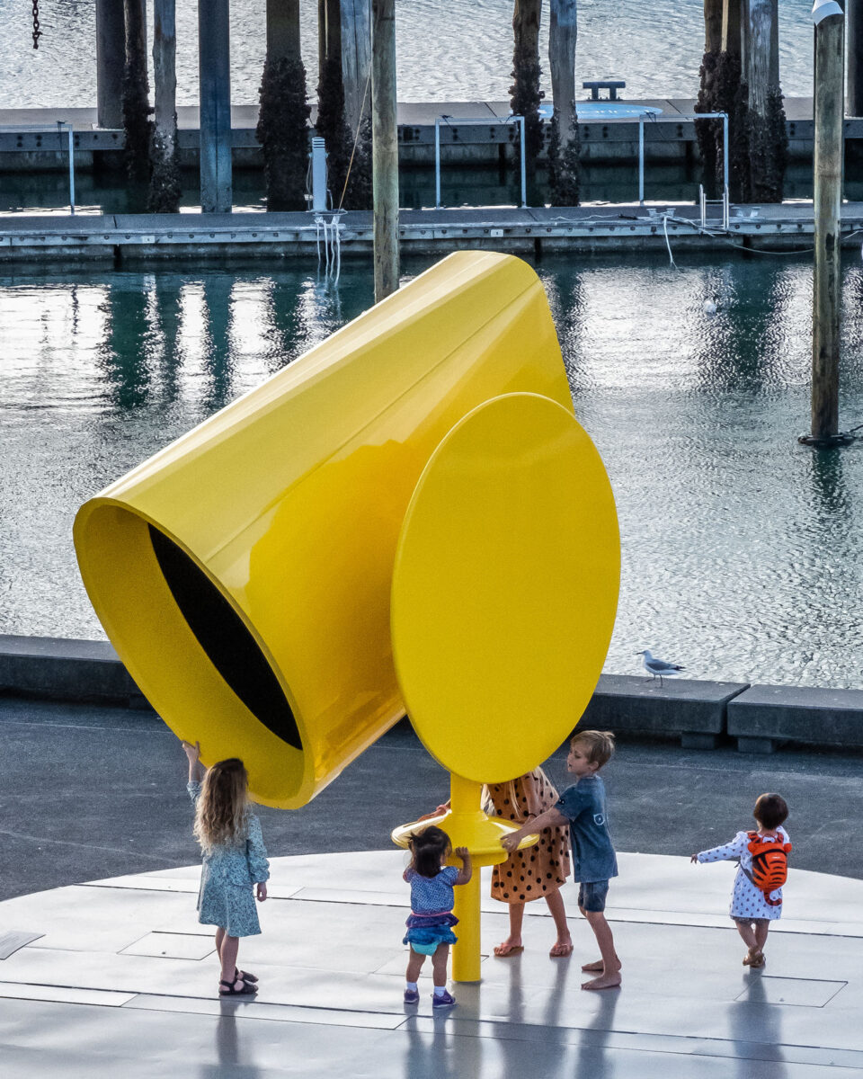 Rainbow Machine, a yellow large scale tube shaped sculpture, with kids interacting with it. 