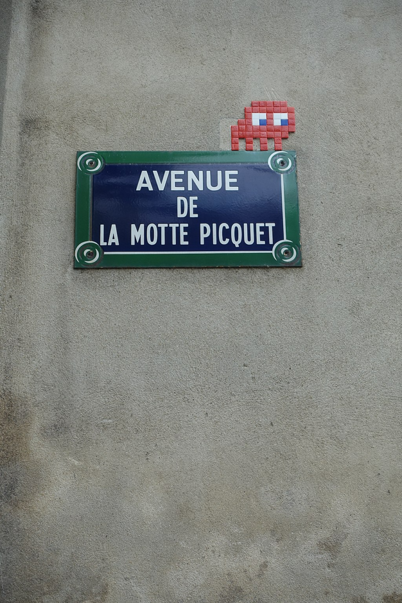 A small space invader mosaic, placed by the artist Invader, perches atop a street sign in Paris. 