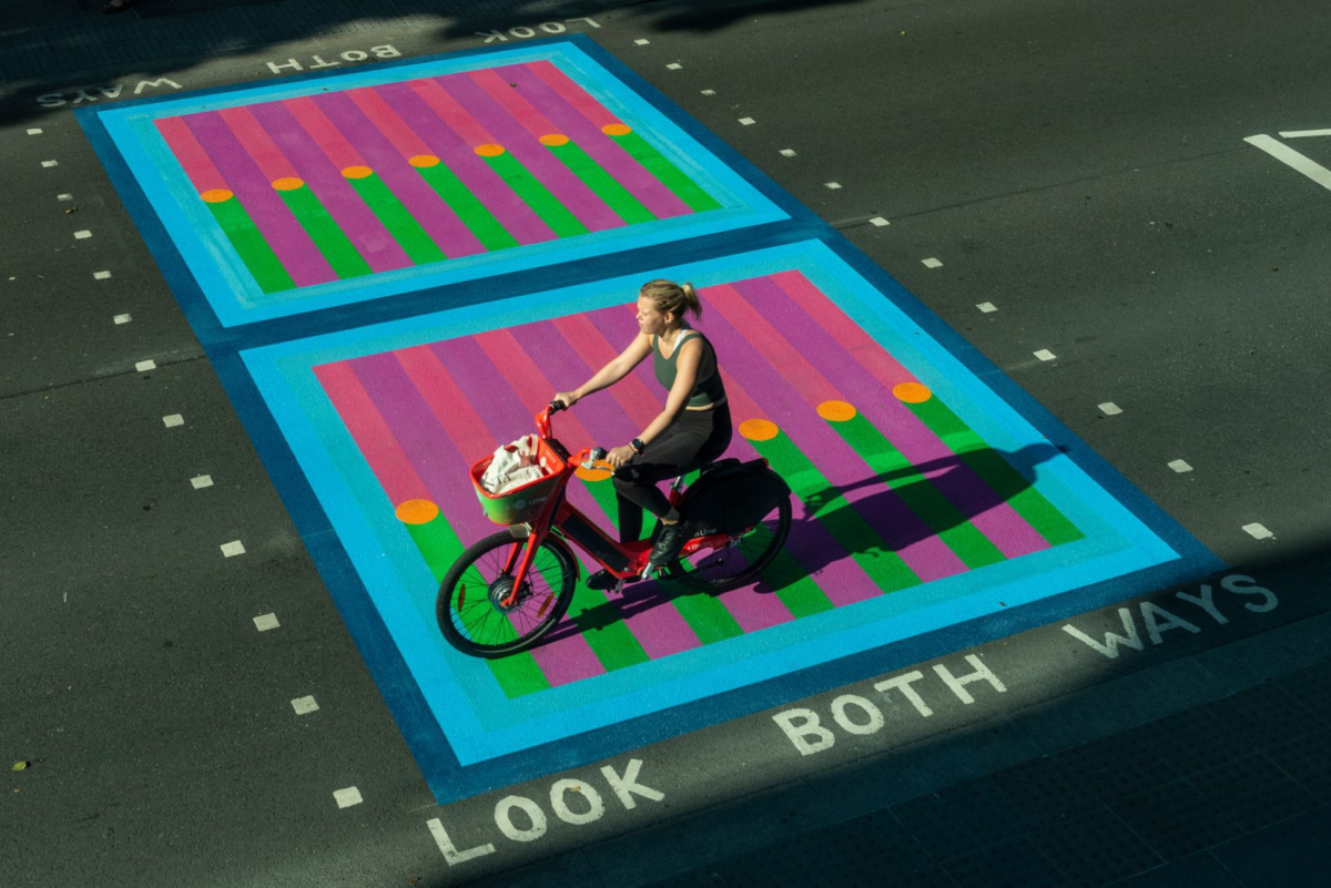 A crosswalk featuring a bright pattern of pink, purple, orange, and green, with a blue border reading "look both ways". 