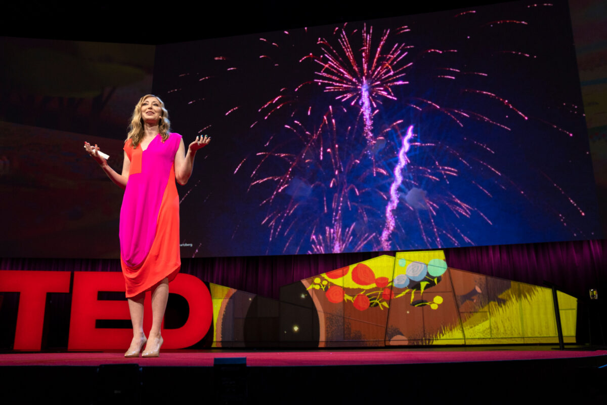 Ingrid Fetell Lee onstage at the TED 2018 conference, wearing an orange and hot pink dress. 