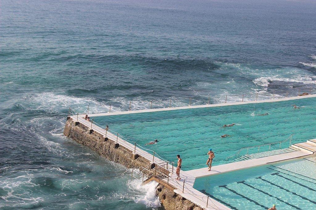 A picture of a turquoise lap pool surrounded on three sides by ocean. 