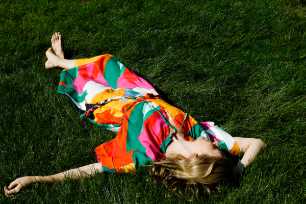 A picture of Ingrid in a multicolored dress lying in the grass. Shot by Belathee.