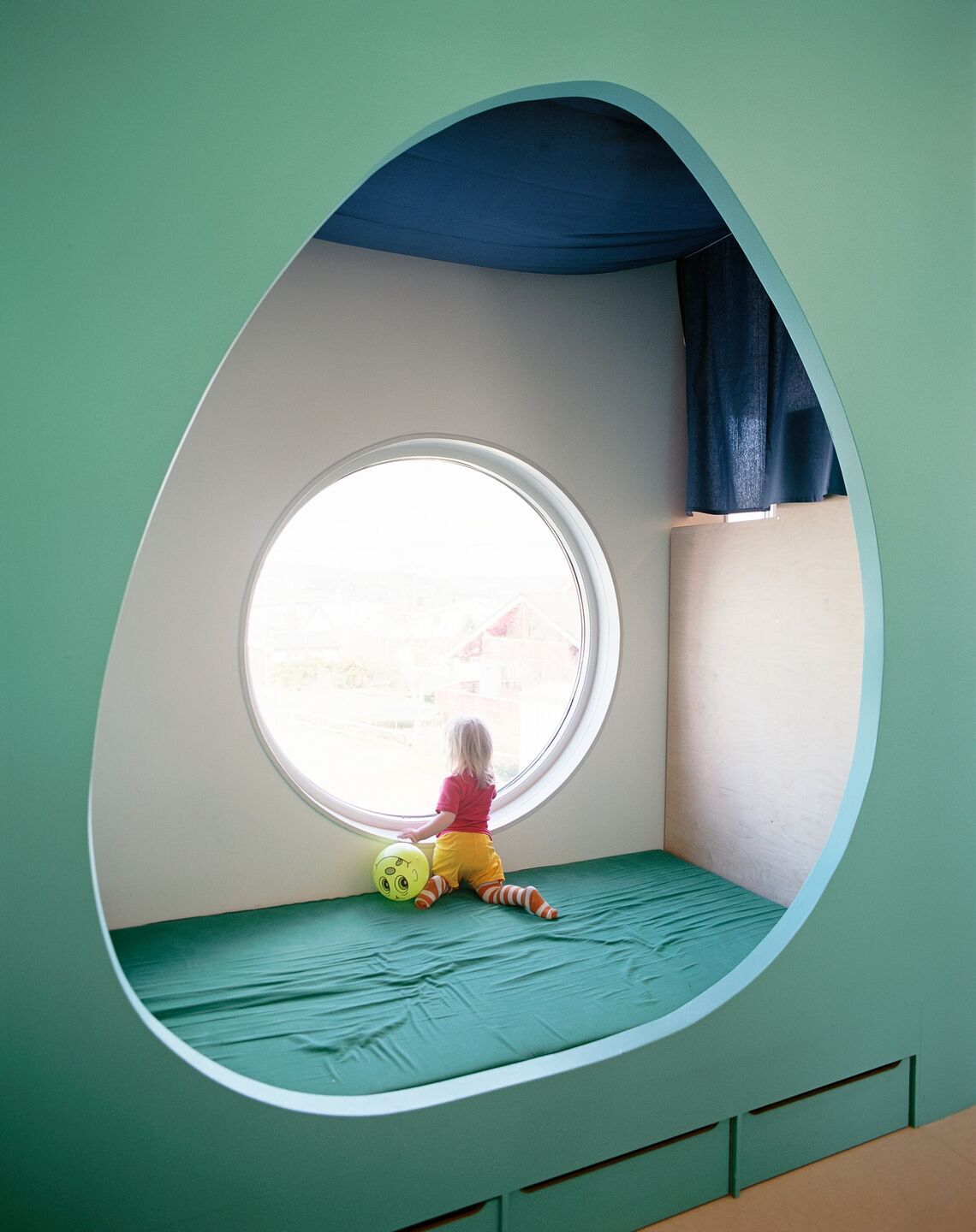 A child peers out of a circular window in an organic-shaped nook.