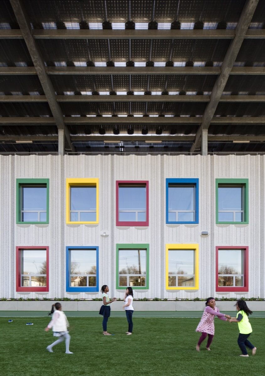 A concrete school building with red, yellow, green, and blue outlines on the windows. 