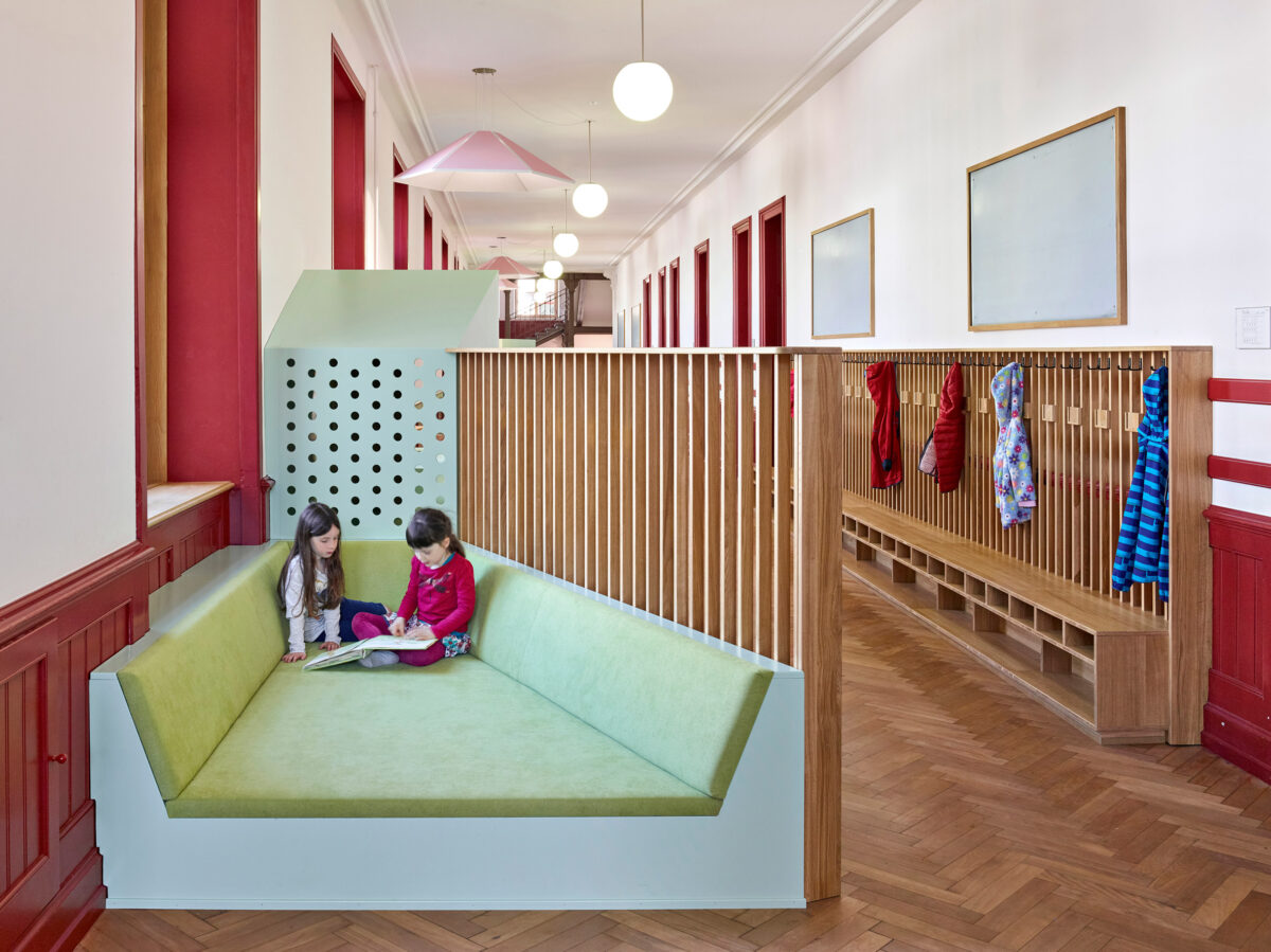 Two children read together in a conversation pit style nook in a hallway. 