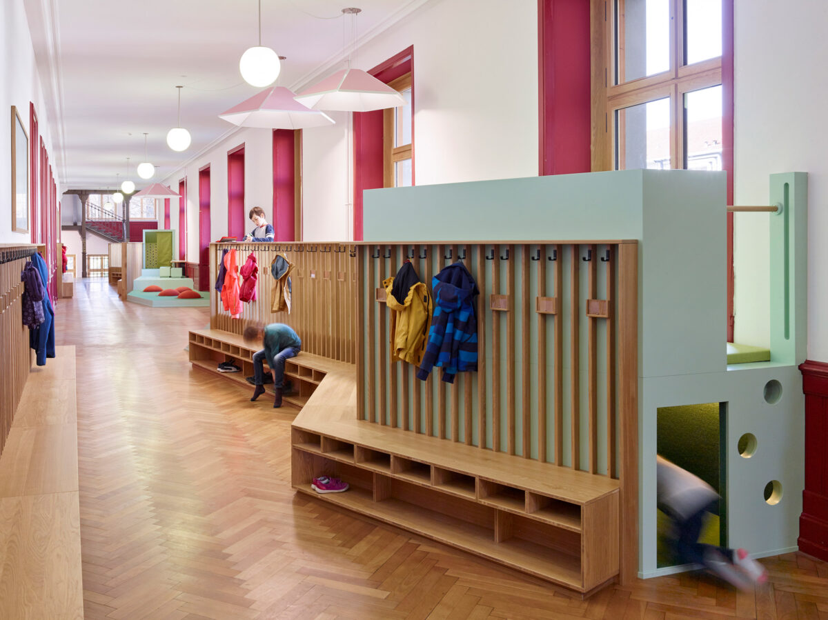 A hallway featuring wood coatracks and play structures integrated. 