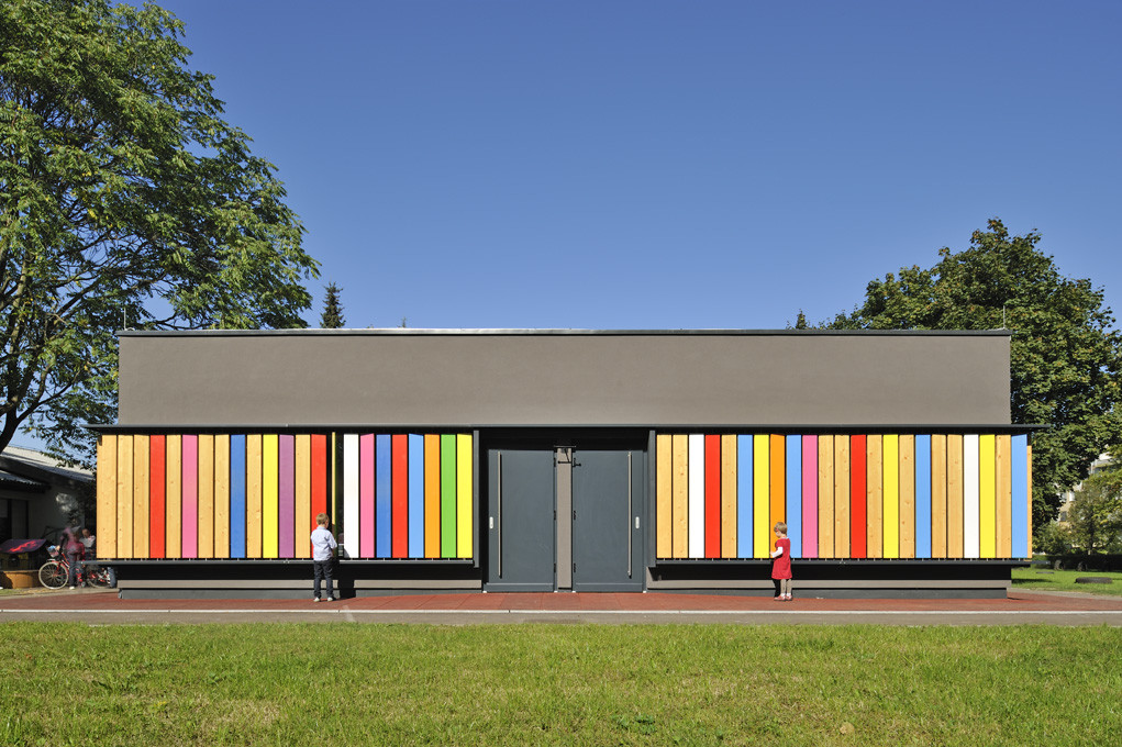A school lined with colorful louvers with children turning the planks to reveal wood on the underside. 