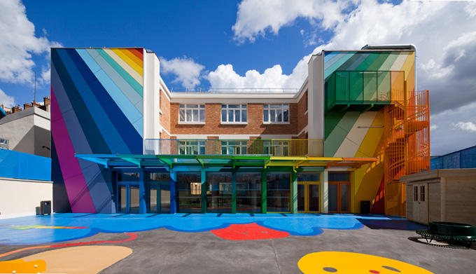 The rear of a school building, painted with rays of bring colors and a rainbow color blocked portico. 