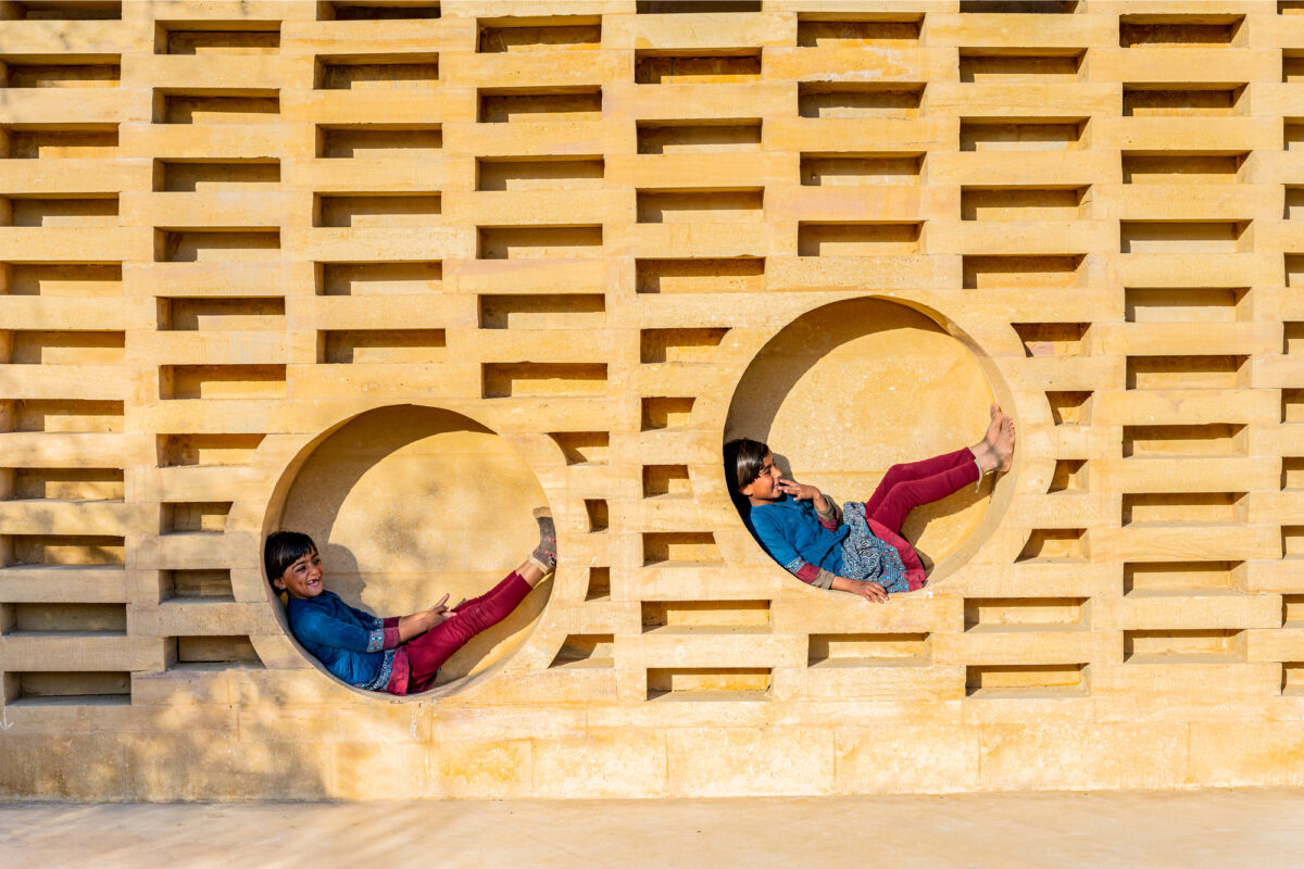 Two children rest in circular nooks cut into the exterior of a building.