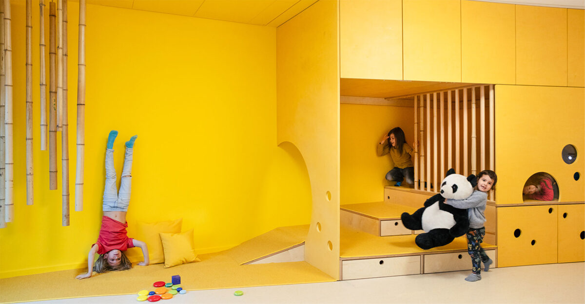 A child does a headstand while others play and hide in a wall structure designed for playing. 