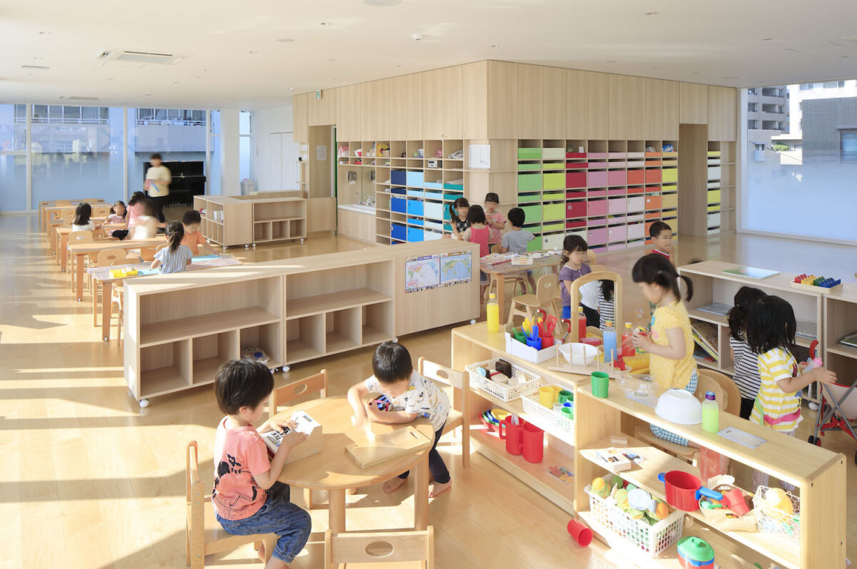 A view of a classroom with children playing, light wood, and colorblocked storage behind. 