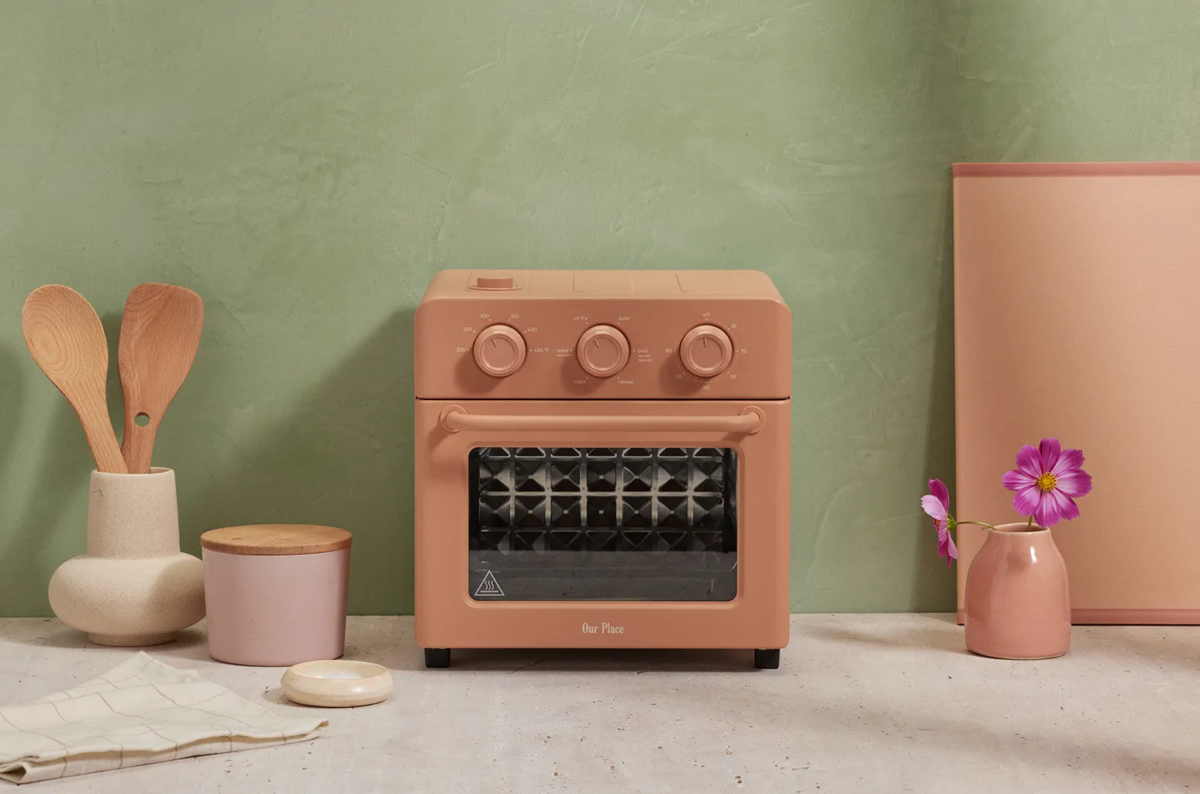 Colorful Tech | A clay pink toaster oven styled with other pink kitchen items like a vase and a jar. 