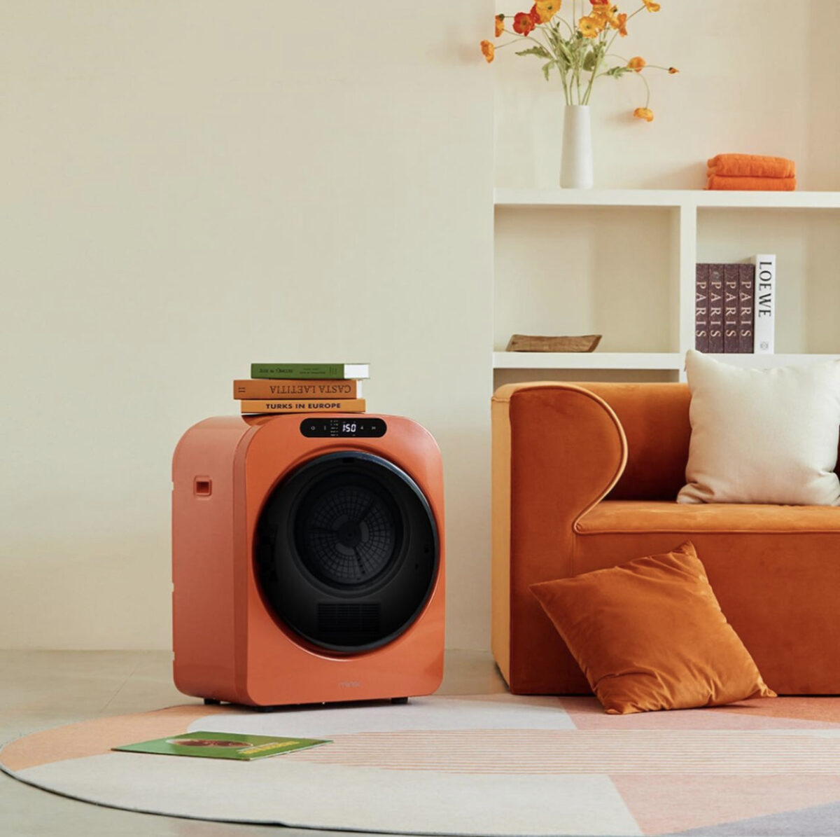 Colorful Tech | A bright orange washing machine styled next to a velvet orange sofa, with books on top. 