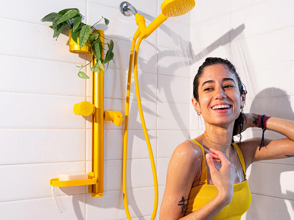 A woman showers under a bright yellow shower head. 