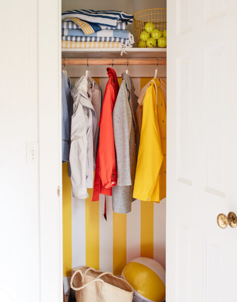 A closet painted with yellow and white cabana stripes with colorful jackets hanging