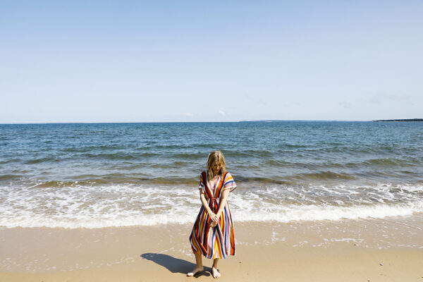 A picture of Ingrid in a striped dress standing in front of the ocean on a beach.